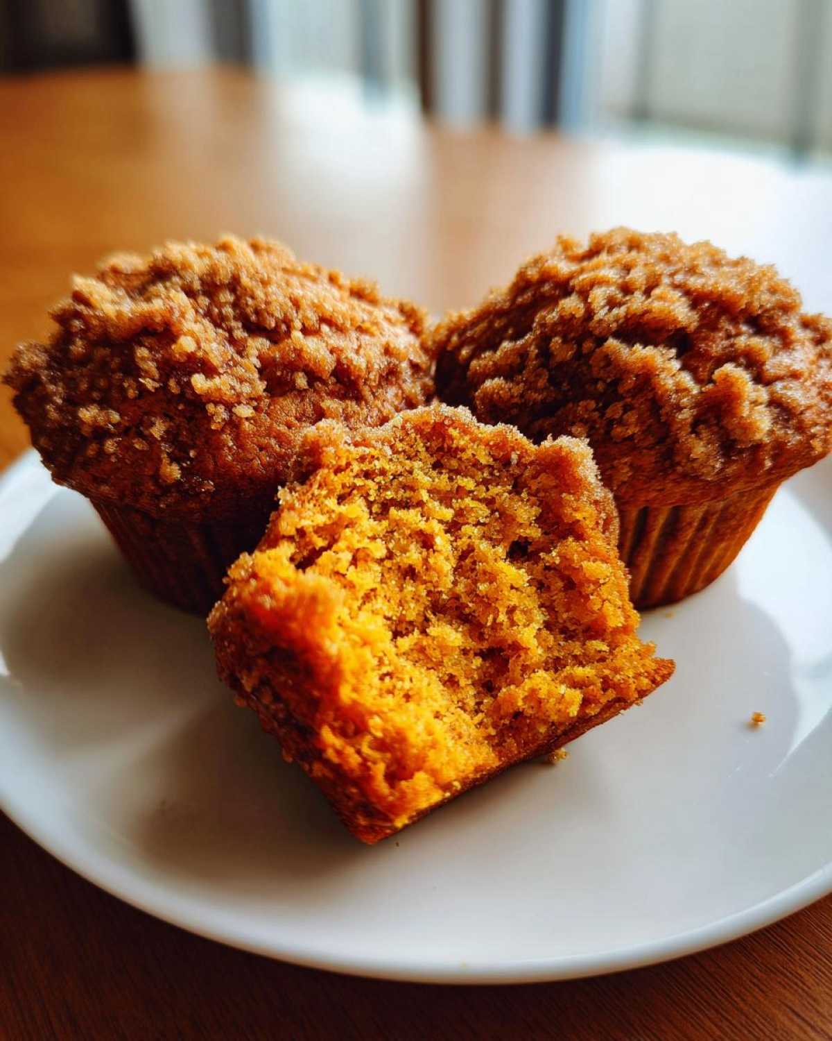 Close-up of three moist sweet potato muffins, one broken open to show the orange interior and crumb topping.