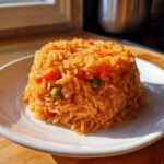 A molded serving of vibrant orange Spanish rice with visible peas and carrots on a white plate.