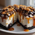 A rich, no-bake Samoa Cheesecake with a thick crust, creamy filling, topped with caramel, chocolate, and toasted coconut.