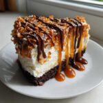 A decadent slice of no-bake Samoa Cheesecake with a chocolate crust, creamy filling, toasted coconut, and heavy drizzles of caramel and chocolate sauce.