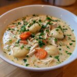 A close-up of a white bowl filled with creamy olive garden chicken gnocchi soup, garnished with fresh parsley.