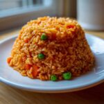 A mound of vibrant orange Spanish rice mixed with bright green peas and diced carrots, served on a white plate.