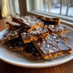 Close-up of stacked pieces of peanut butter pretzel bark topped with dark chocolate and flaky sea salt.