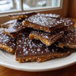 A stack of homemade peanut butter pretzel bark squares topped with dark chocolate and flaky sea salt.