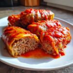 Close-up of four savory cabbage rolls stuffed with meat and rice, smothered in thick tomato sauce on a white plate.