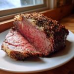 Close-up of a thick slice of medium-rare rib roast showing a deep pink center and a heavily seasoned crust.