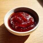 Close-up of thick, dark red homemade bbq sauce served in a small white ramekin on a wooden surface.