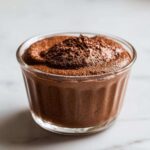 A single serving of rich, dark chocolate mousse topped with cocoa powder in a clear glass dish.