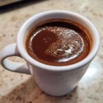 Close-up of a rich, dark french hot chocolate with foam in a white ceramic mug.