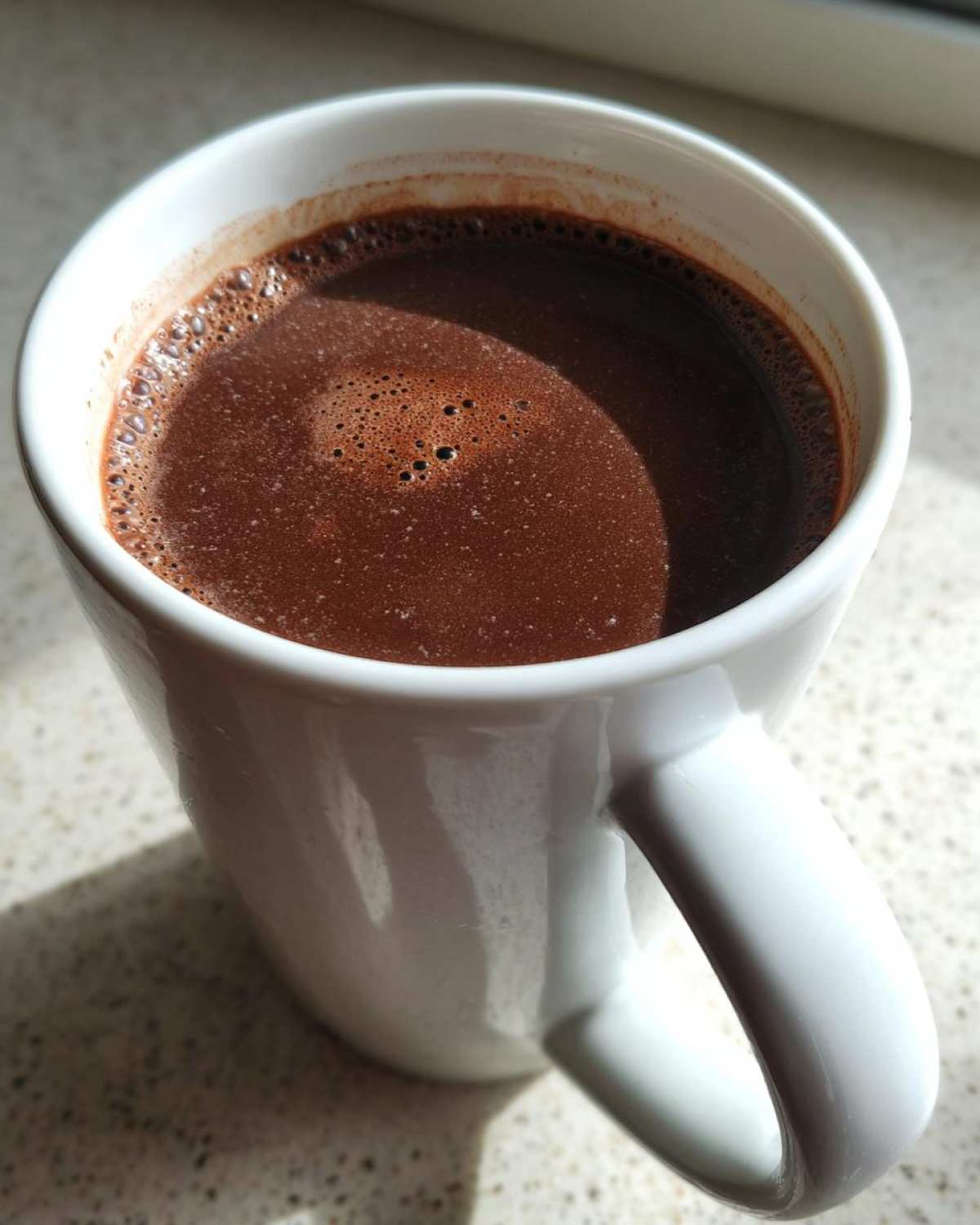 Close-up of a rich, dark french hot chocolate with small bubbles on the surface, served in a white ceramic mug.