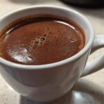 Close-up of a rich, dark brown french hot chocolate with small bubbles on the surface, served in a white ceramic mug.