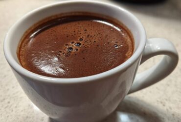 Close-up of a rich, dark brown french hot chocolate with small bubbles on the surface, served in a white ceramic mug.