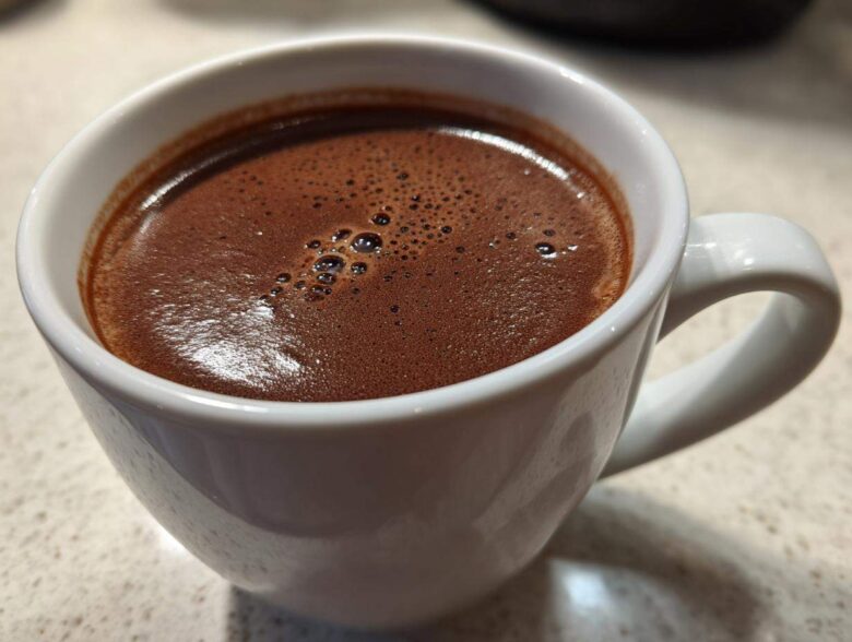 Close-up of a rich, dark brown french hot chocolate with small bubbles on the surface, served in a white ceramic mug.