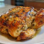 A whole, perfectly roasted spatchcock chicken with crispy, golden-brown skin seasoned with herbs, resting on a white plate.