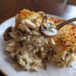 A spoonful of creamy chicken wild rice casserole featuring mushrooms and a crispy topping.