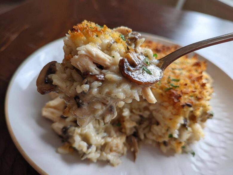 A spoonful of creamy chicken wild rice casserole featuring mushrooms and a crispy topping.