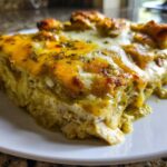 Close-up of a rich, cheesy slice of green chile chicken enchiladas covered in melted cheese and herbs.