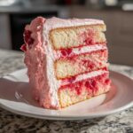 A tall slice of layered cherry cake featuring white sponge layers, bright red cherry filling, and pink buttercream frosting.