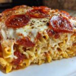 Close-up of a thick slice of pizza pasta bake showing melted cheese, pepperoni, and spiral pasta.