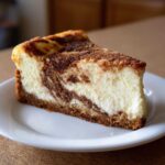 A close-up of a perfect slice of snickerdoodle cheesecake showing the creamy filling and cinnamon swirl topping.