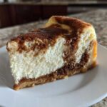 A close-up shot of a single slice of snickerdoodle cheesecake with a cinnamon swirl on a white plate.