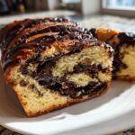 A close-up of a soft chocolate babka loaf, sliced to show the rich chocolate swirl inside, drizzled with glaze.