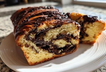A close-up of a soft chocolate babka loaf, sliced to show the rich chocolate swirl inside, drizzled with glaze.