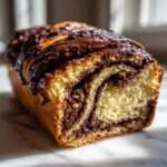 A close-up, cross-section view of a freshly baked chocolate babka loaf showing soft, swirled layers and a rich chocolate glaze.
