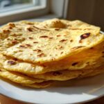 A stack of warm, freshly cooked soft corn tortillas with light char marks resting on a white plate.