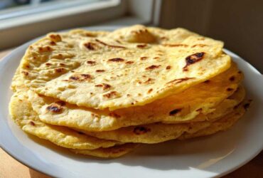A stack of warm, freshly cooked soft corn tortillas with light char marks resting on a white plate.
