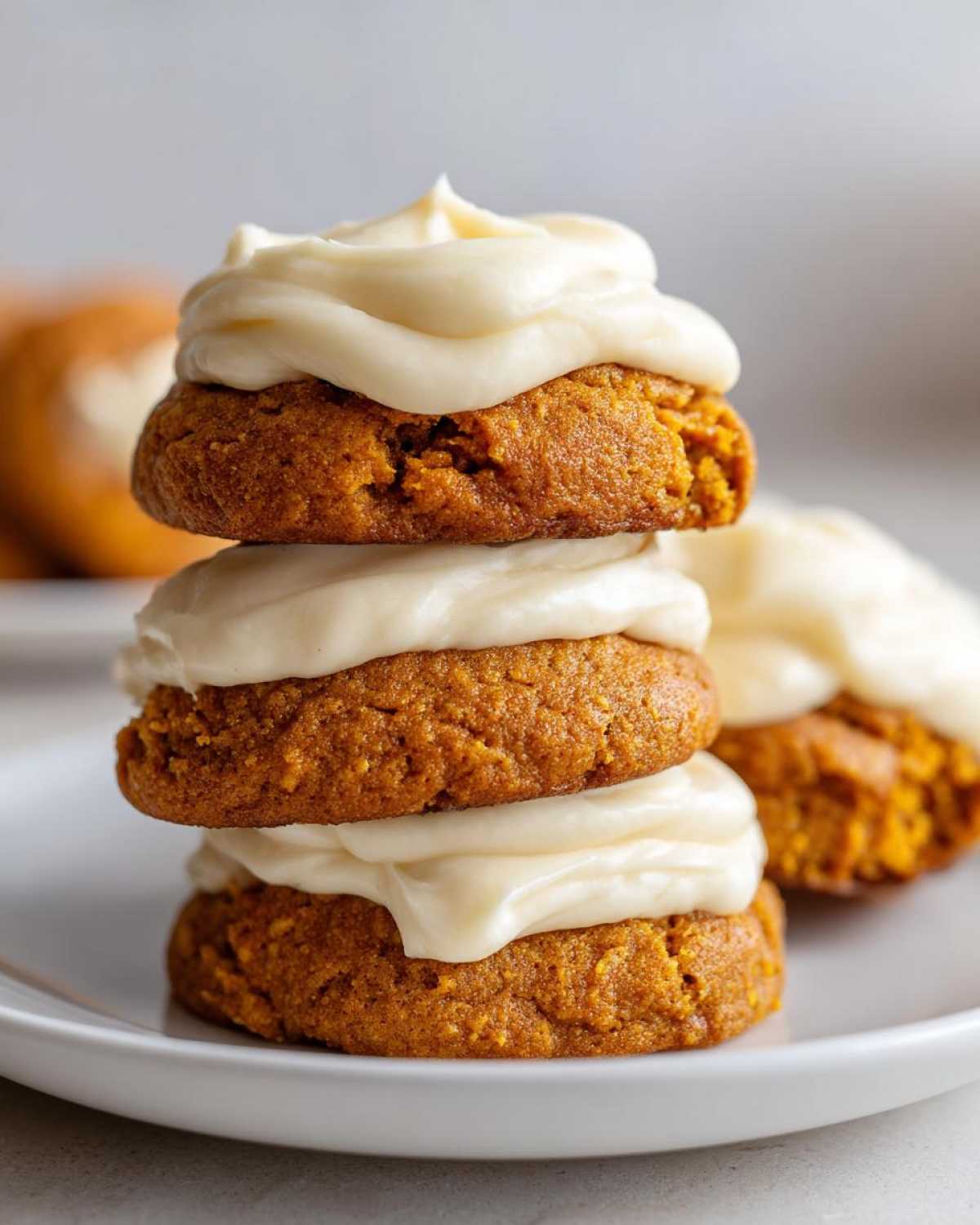 A stack of three soft pumpkin cookie halves layered with thick cream cheese frosting.