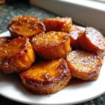 A close-up of several thick slices of glistening, caramelized southern candied yams piled on a white plate.