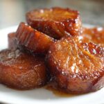 A close-up stack of thick, glossy, caramelized slices of southern candied yams resting on a white plate.