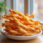 A close-up of a white bowl filled with golden, twisted, spicy cheese straws.