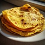 A stack of golden yellow, soft corn tortillas with light char marks resting on a white plate.