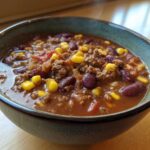Close-up of a steaming bowl of rich crockpot cowboy soup featuring ground beef, kidney beans, and bright yellow corn kernels.