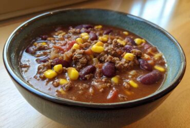 Close-up of a steaming bowl of rich crockpot cowboy soup featuring ground beef, kidney beans, and bright yellow corn kernels.