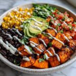 A vibrant sweet potato taco bowl featuring roasted sweet potatoes, black beans, corn, pico de gallo, avocado, and a creamy drizzle.