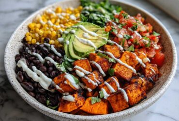 A vibrant sweet potato taco bowl featuring roasted sweet potatoes, black beans, corn, pico de gallo, avocado, and a creamy drizzle.
