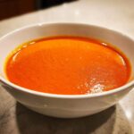 Close-up of a rich, velvety tomato bisque with a vibrant orange-red color served in a white bowl.