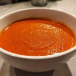 Close-up of rich, velvety tomato bisque, bright orange-red, served in a white bowl.