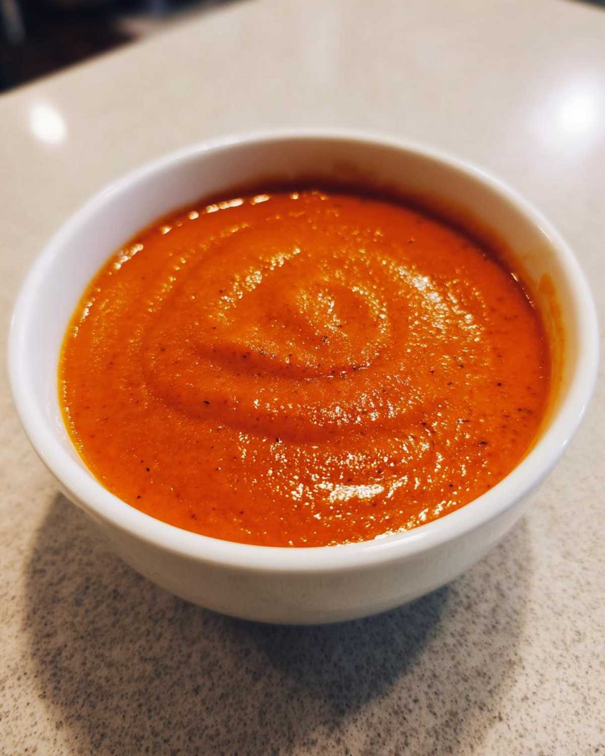 Close-up of a small white bowl filled with rich, bright orange tomato bisque, showing a smooth, velvety texture.