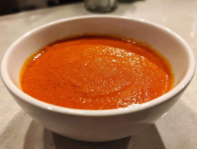 Close-up of rich, velvety tomato bisque, bright orange-red, served in a white bowl.