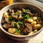 Close-up of a bowl containing white bean mushroom stew mixed with gnocchi, topped with fresh parsley.