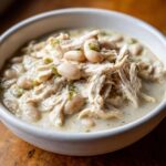 A close-up of a hearty bowl of white chicken chili recipe, featuring shredded chicken and white beans in a creamy sauce.