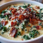 Close-up of a bowl of creamy Zuppa Toscana soup garnished generously with crispy bacon bits and grated Parmesan cheese.