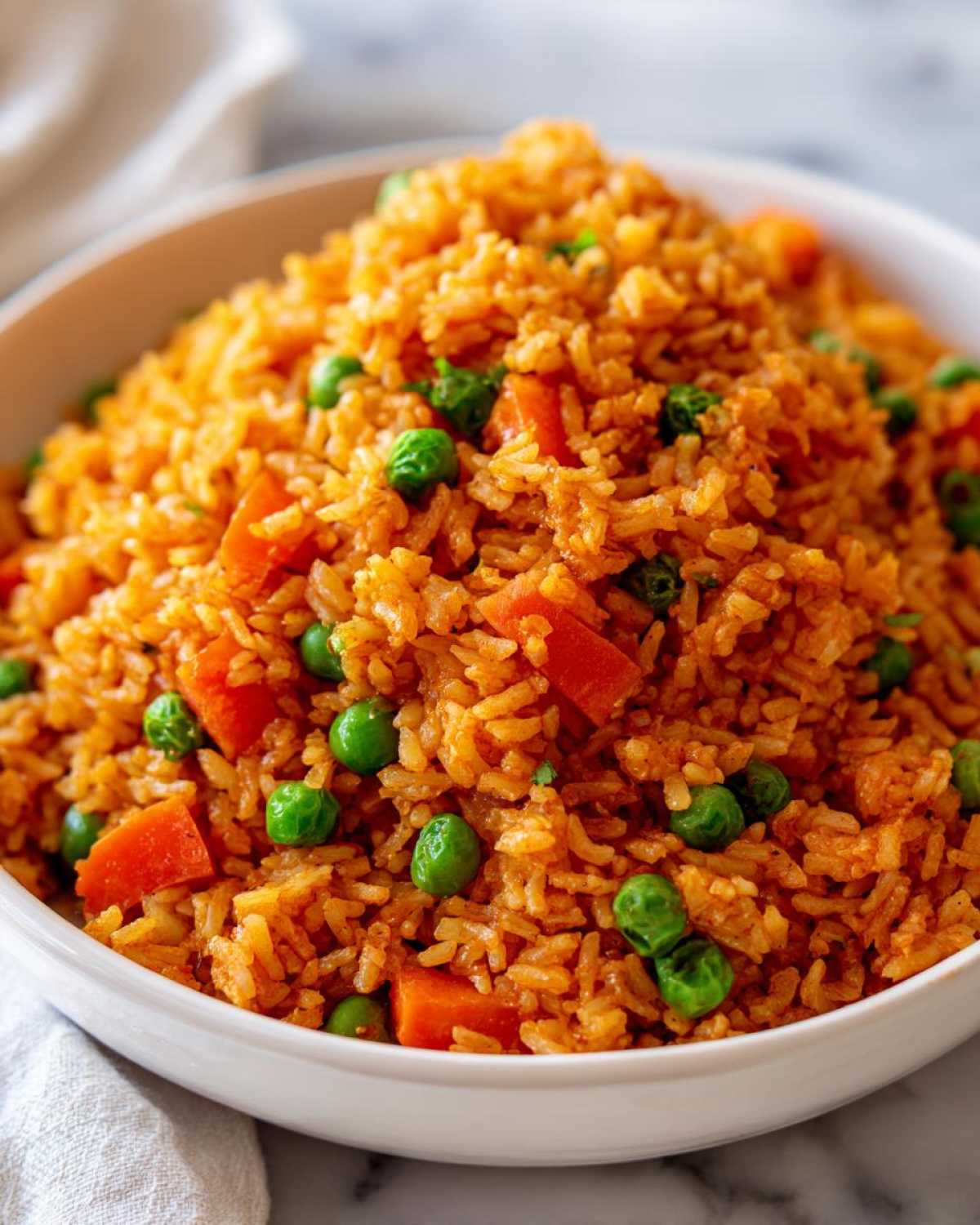 Close-up of a white bowl filled with vibrant, orange-colored spanish rice mixed with bright green peas and diced carrots.