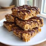 A stack of homemade, no-bake protein bars made with oats and drizzled generously with melted chocolate.