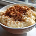 A close-up of creamy rice pudding in a white bowl, generously dusted with cinnamon.