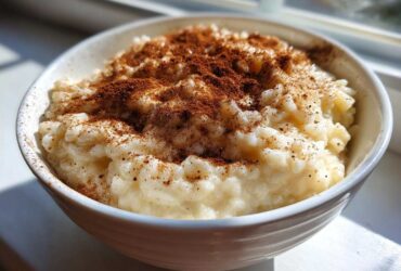 A close-up of creamy rice pudding in a white bowl, generously dusted with cinnamon.